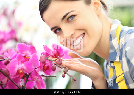 Donna sorridente nel giardino di fiori toccare un'orchidea Foto Stock