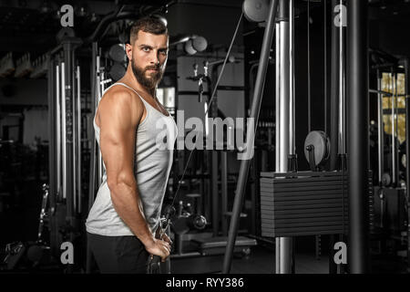 Bodybuilding. Uomo Barbuto doingcable permanente braccio rettilineo pulldown in palestra guarda fiducioso della fotocamera Foto Stock