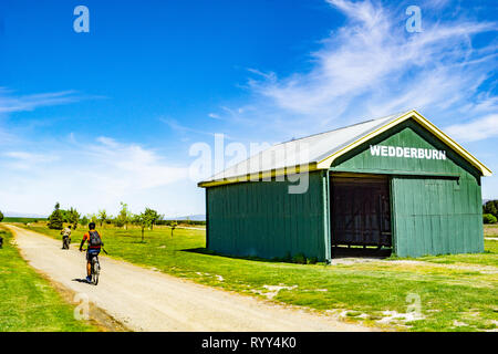 WEDDERBURN NUOVA ZELANDA - Ottobre 22 2018; su Central Otago Rail Trail ciclisti passando il vecchio punto di riferimento verde capannone ferroviario Foto Stock