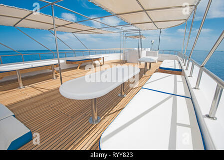 Area solarium di un grande luxury motor yacht con sedie tavolo divano e tropicale vista mare sullo sfondo Foto Stock