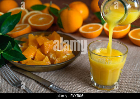 Arance a fette, foglie d'arancio e bicchiere di succo di arancia su un tavolo da cucina con sfondo rustico Foto Stock