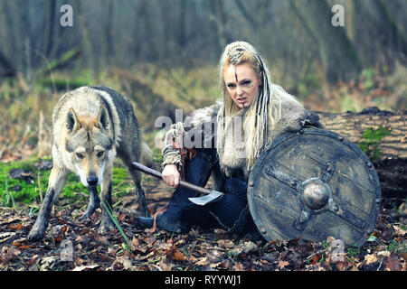 Bella viking warrior woman in tradizionali abiti del guerriero, con ax e la protezione, accanto ad un lupo selvatico, pronti ad attaccare Foto Stock