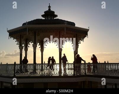 Stagliano forme delle persone che ballano sul lungomare di Brighton bandstand al tramonto, East Sussex, Inghilterra Foto Stock