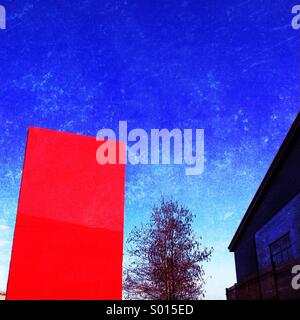 Segno rosso post, albero e unità industriali contro screziato azzurro del cielo Foto Stock