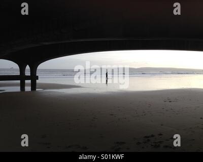 L'uomo la caccia al tesoro usando un rivelatore di metalli sulla spiaggia sotto il molo di Bournemouth Foto Stock