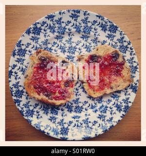 Jam su due metà tostato di una hot cross bun, su un vintage blu e bianco piastra floreali. Foto Stock