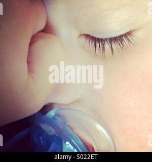 Close-up di un bambino che dorme con un manichino blu succhietto nella sua bocca. Foto Stock