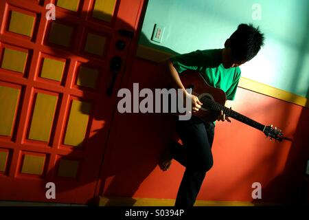 Giovani asiatici teen suonando la chitarra in un vuoto di soggiorno Foto Stock