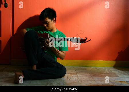 Giovani asiatici teen suonando la chitarra in un vuoto di soggiorno Foto Stock