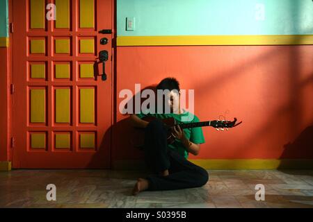 Giovani asiatici teen suonando la chitarra in un vuoto di soggiorno Foto Stock