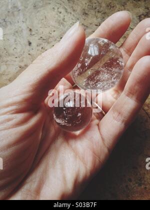 Femmina di mano che regge due quarzo trasparente sfera di cristallo sulla tavola di legno. Foto Stock