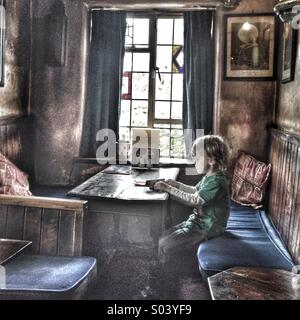 Ragazzo seduto sul suo proprio in corrispondenza di una tabella in un vecchio pub Foto Stock