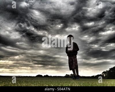 Silhouette di un ragazzo contro il cielo in tempesta Foto Stock