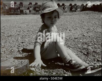 Little Boy in hat giocando sulla spiaggia di ciottoli di Whitstable Kent REGNO UNITO Foto Stock