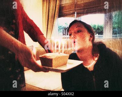 Donna soffiando fuori candele su una piccola torta di compleanno Foto Stock