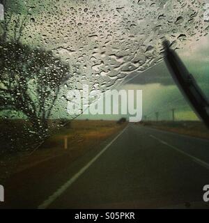 La pioggia su di un parabrezza di automobile durante la guida lungo un outback road in Australia Foto Stock