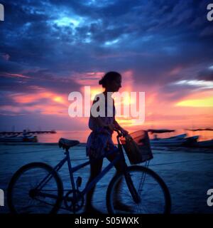 La donna corse in bicicletta in spiaggia al tramonto a Holbox island, Quintana Roo, la penisola dello Yucatan, Messico Foto Stock