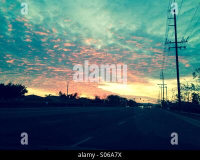 Vivid caldo tramonto riflette increspata nuvole sopra un lungo vuoto suburban street in California. Foto Stock