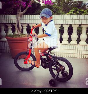 Po' eurasian boy è in bicicletta con la sua bicicletta su una terrazza Foto Stock