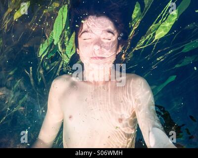 Ragazzo immerso in un fiume puro con vegetazione lussureggiante Foto Stock