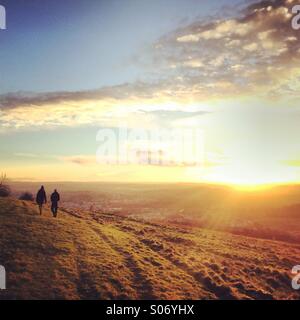 Distante walkers prendendo una Domenica nel tardo pomeriggio passeggiata come il sole proietta raggi oltre la periferia della città di Bath Foto Stock