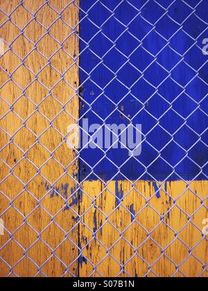 Giallo e blu abstract urban texture. Dipinto di pannelli in legno dietro una recinzione ad anelli. Foto Stock