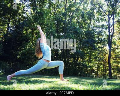 Una donna fare yoga al di fuori nel prato circondato dalla natura. Foto Stock