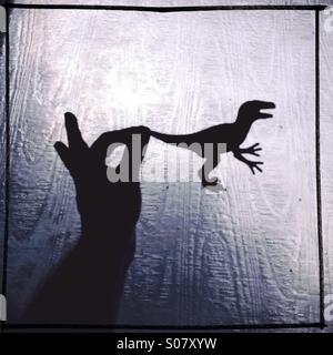 Silhouette di una mano che tiene un dinosauro giocattolo , soft focus immagine Foto Stock