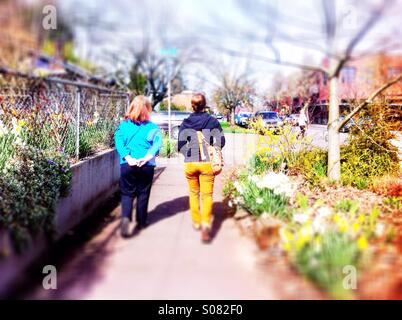 Due donne a camminare sul marciapiede in primavera Foto Stock