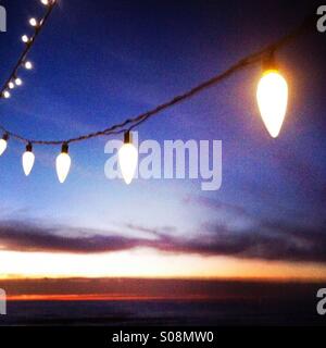 Illuminato di vacanze/luci di Natale appendere con il sole che tramonta sullo sfondo. Manhattan Beach, California USA. Foto Stock