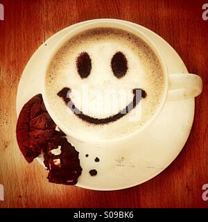 Pausa caffè - un cappuccino con una faccina sorridente e un cookie biscotto Foto Stock