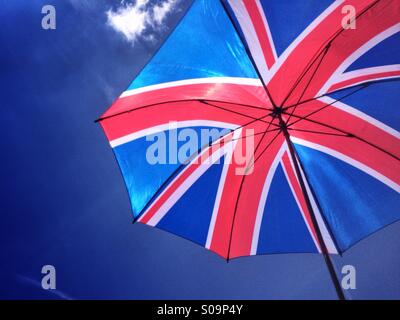 Il sole splende attraverso un ombrello con un design dell'Unione Bandiera della Gran Bretagna, contro un luminoso cielo blu su un giorno d'estate. Foto Stock