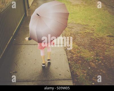 Piccola ragazza camminare sotto un ombrello. Foto Stock