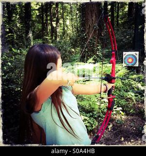 Una ragazza di 10 anni mira una freccia in corrispondenza di un target nella foresta. Foto Stock