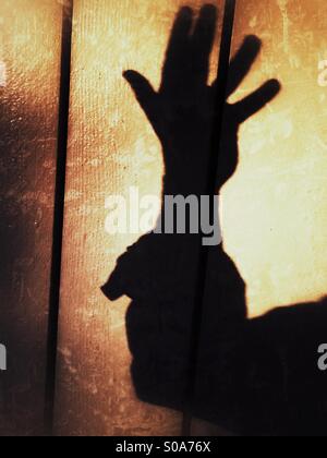 Un uomo getta un' ombra sul muro, contando sulla sua mano. Numero cinque. Foto Stock