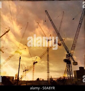 Doppio esposto e riflessa foto di gru su un sito di costruzione contro un arancio skyline, in Colindale, Londra, Inghilterra. Foto Stock