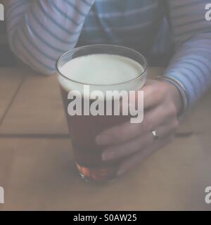 Premendo immagine guardando attraverso una nebbia a donna tenendo la pinta di birra in casa pubblica Foto Stock