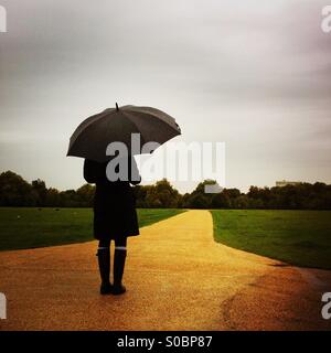 Una donna si erge in Hyde Park in un giorno di pioggia. London, England Regno Unito. Foto Stock