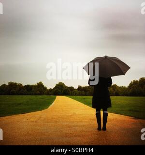 Una donna si erge in Hyde Park in un giorno di pioggia. London, England Regno Unito. Foto Stock