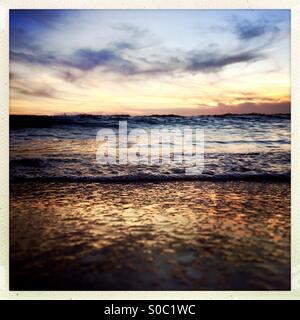 Un'onda rotoli sulla spiaggia al tramonto. Cardiff dal mare, San Diego, California USA. Foto Stock