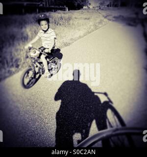 A sette anni di vecchio ragazzo corse la sua bicicletta da un uomo su una pista ciclabile. Foto Stock