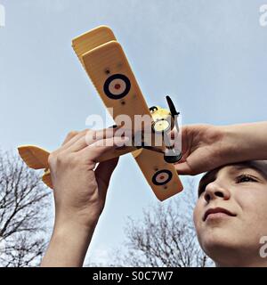 Ragazzo tenendo il suo modello biplano contro il cielo Foto Stock