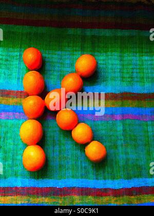 K dipinto composto da veri e freschi kumquat su un colorato tappeto di bambù. La lettera K per kumquat. Modo creativo di imparare l'alfabeto. Istruzione innovativa. Foto Stock
