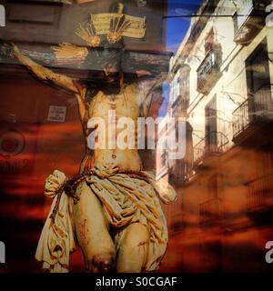 Immagine di Gesù Cristo crocifisso decora una finestra per la Settimana di Pasqua con la riflessione di una strada di Cadice, Andalusia, Spagna Foto Stock