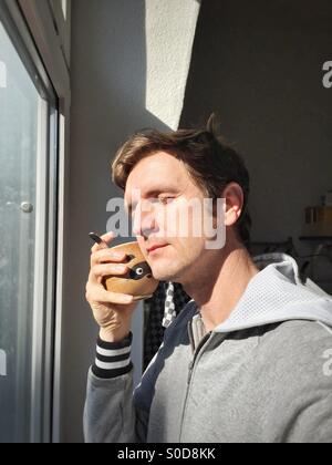 Giovane uomo caucasico in casuale di bere il caffè caldo accanto alla finestra Foto Stock