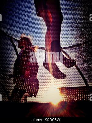 Due ragazze rimbalzare sul trampolino retroilluminati da sole di sera Foto Stock