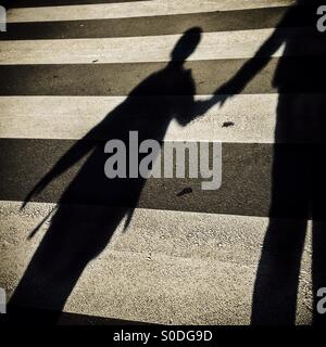 Ombra di un bambino e suo padre attraversando un passaggio pedonale Foto Stock