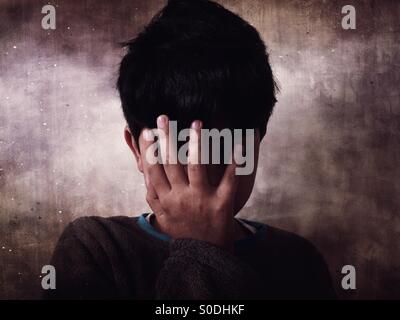 Ragazzo miserabile nascondendo la faccia con la mano Foto Stock