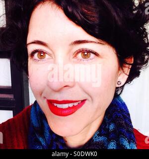Donna che indossa un rossetto rosso con sciarpa blu e rosso coat sorridente a un amico Foto Stock