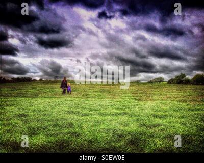 La madre e il bambino a piedi attraverso il campo contro un cielo tempestoso Foto Stock